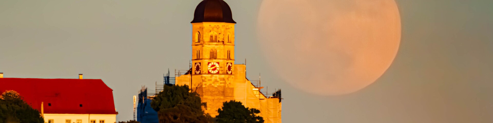 A church with a clock tower and a large moon in the sky.