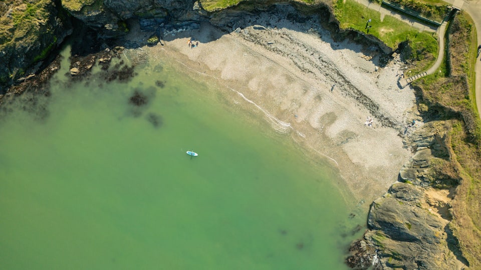 A coastal area with a greenish sea, rocky cliffs, and a path along the shore.