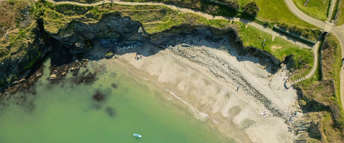 A coastal area with a greenish sea, rocky cliffs, and a path along the shore.