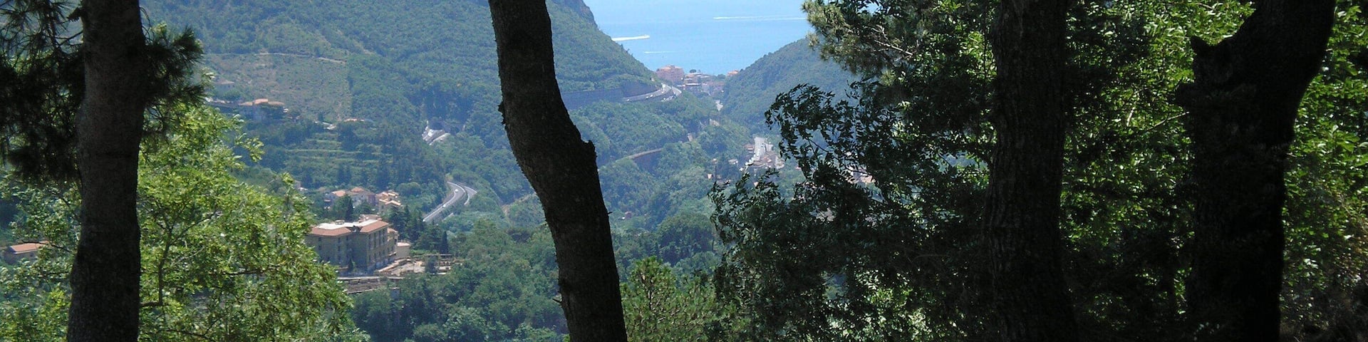 A mountainous landscape with dense forests and a winding road leading to a coastal area.