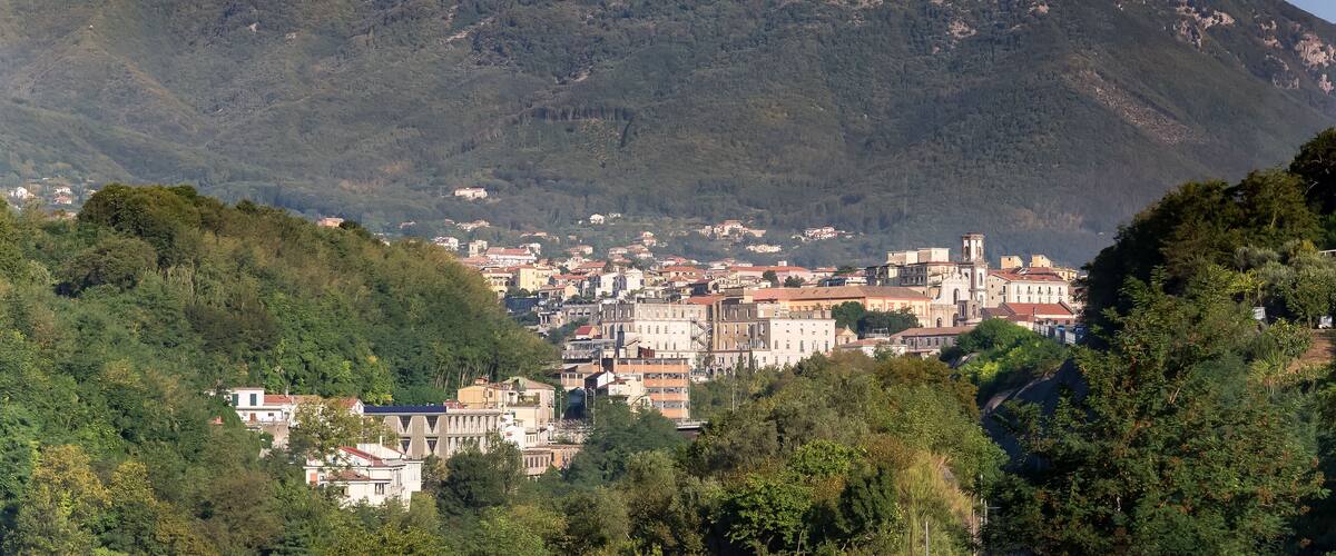A town nestled at the base of a mountain with a prominent church and a transmission tower on the peak.