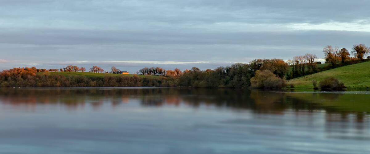 A calm lake with a reflection of trees and hills.