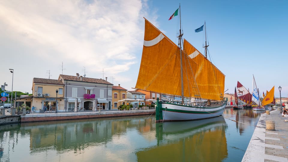A canal with boats, buildings, and flags.