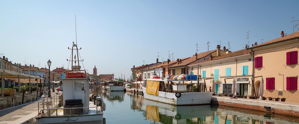 Un canal bordé de bateaux amarrés, des bâtiments aux volets rouges et un ciel dégagé.