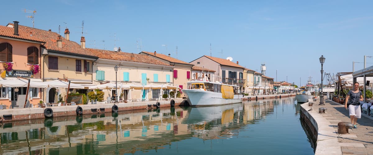 A canal with boats, waterfront buildings, and a pedestrian walkway.