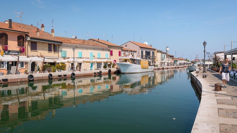 Un canale con barche, edifici sul lungofiume e una passeggiata pedonale.