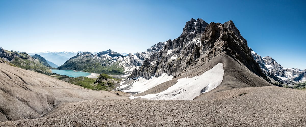 A rugged mountain landscape with a prominent rocky peak, a glacier, and a turquoise lake in the background.