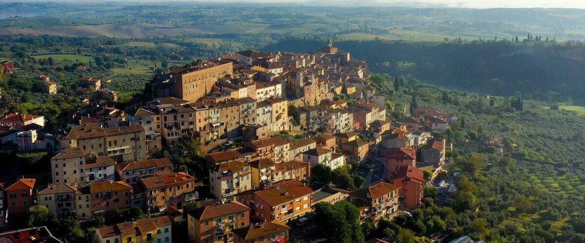 A historic town with a prominent castle on a hill, surrounded by lush green fields and rolling hills in the background.