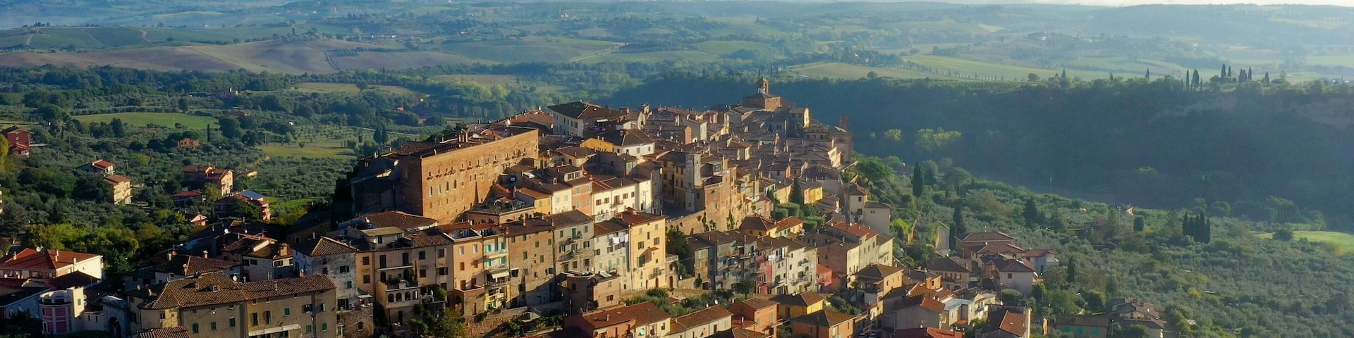 A historic town with a prominent castle on a hill, surrounded by lush green fields and rolling hills in the background.