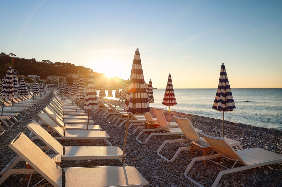 A beach with rows of sun loungers and striped beach umbrellas.