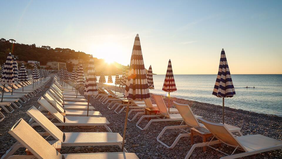 A beach with rows of sun loungers and striped beach umbrellas.