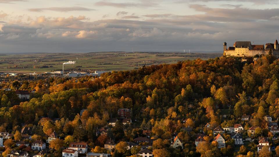 A castle on a hill with autumn foliage, surrounded by a village.