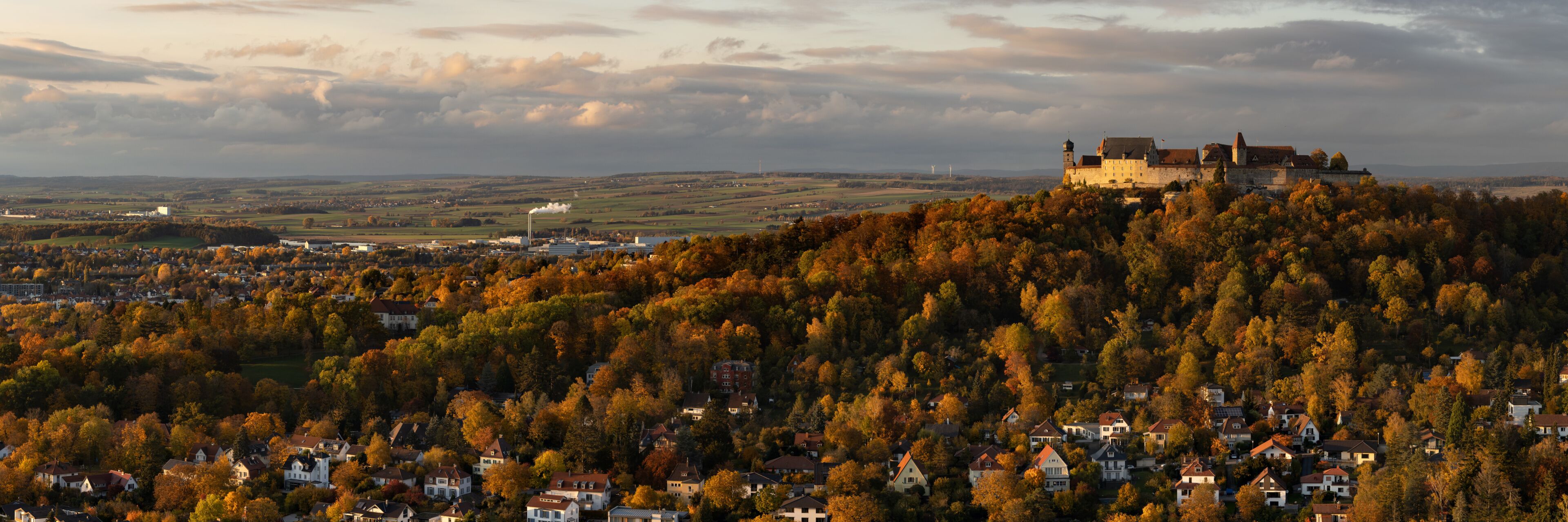 A castle on a hill with autumn foliage, surrounded by a village.