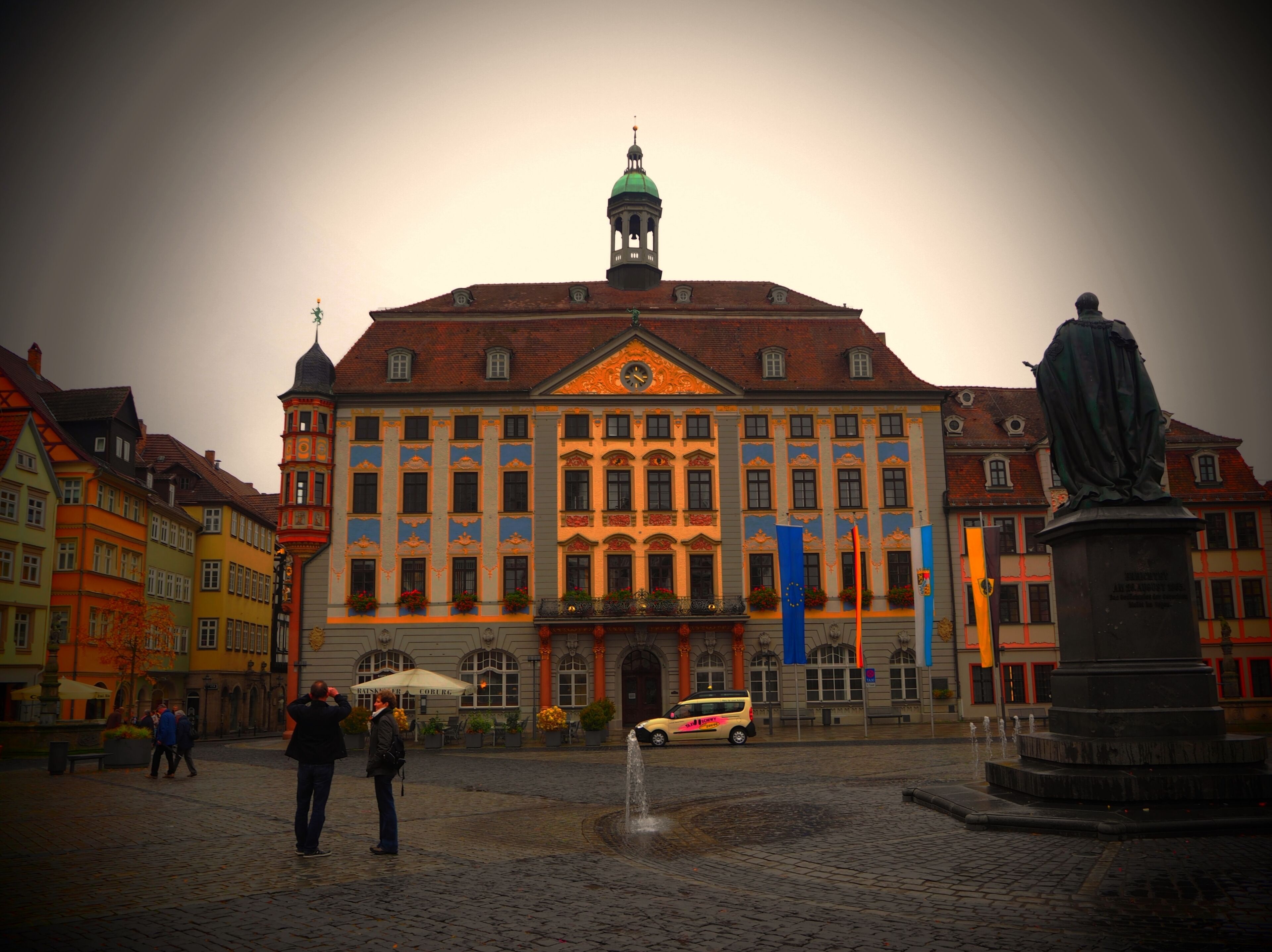 A historic building with a green dome and a statue in front.