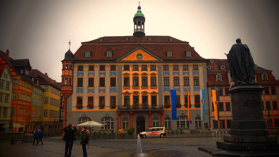 A historic building with a green dome and a statue in front.