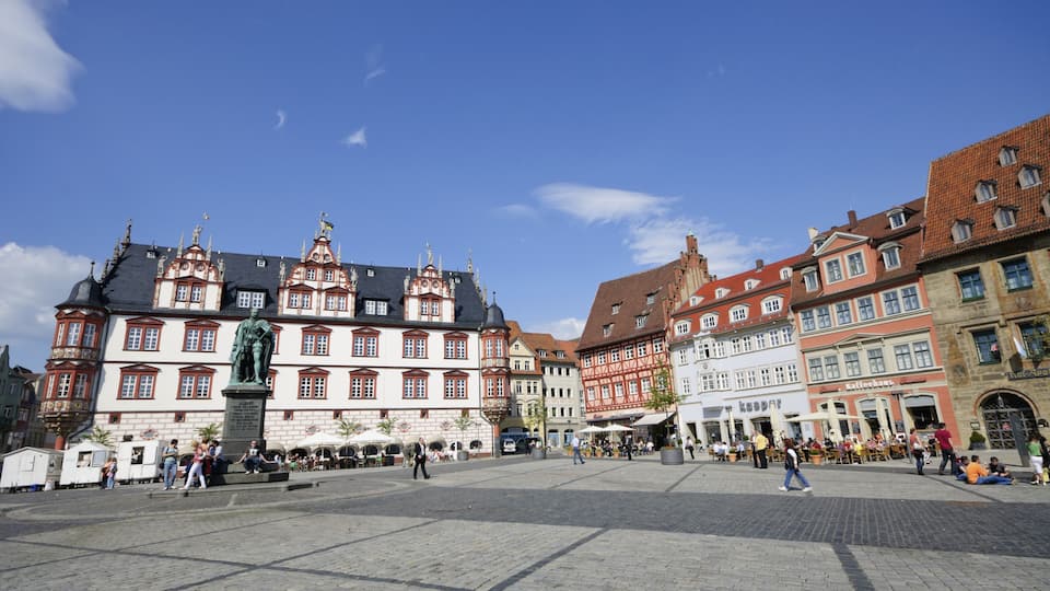 A historic European square with cobblestone pavement, ornate buildings, and a statue.