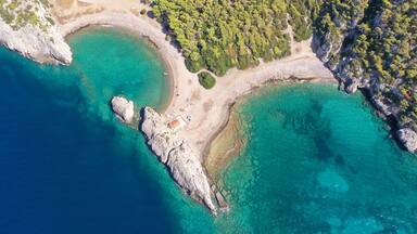 Vue aĂ©rienne dâune zone cĂŽtiĂšre avec des eaux turquoise limpides, des rivages rocheux et un petit bĂątiment situĂ© prĂšs du bord de lâeau.