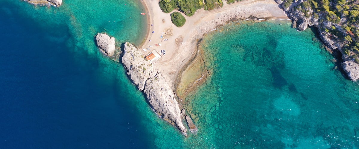 A coastal landscape with clear turquoise waters, rocky outcrops, and a small building near the shore.