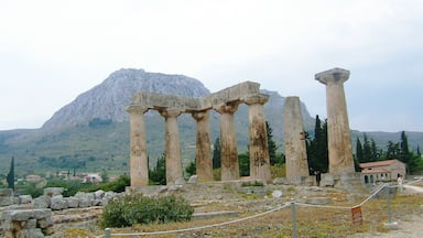 Ancient ruins with columns, a mountain in the background, and a village below.