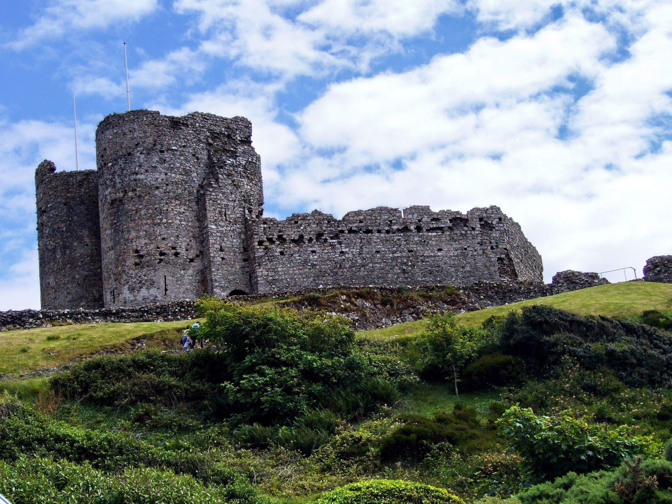 A historic stone castle on a grassy hill with a clear sky.