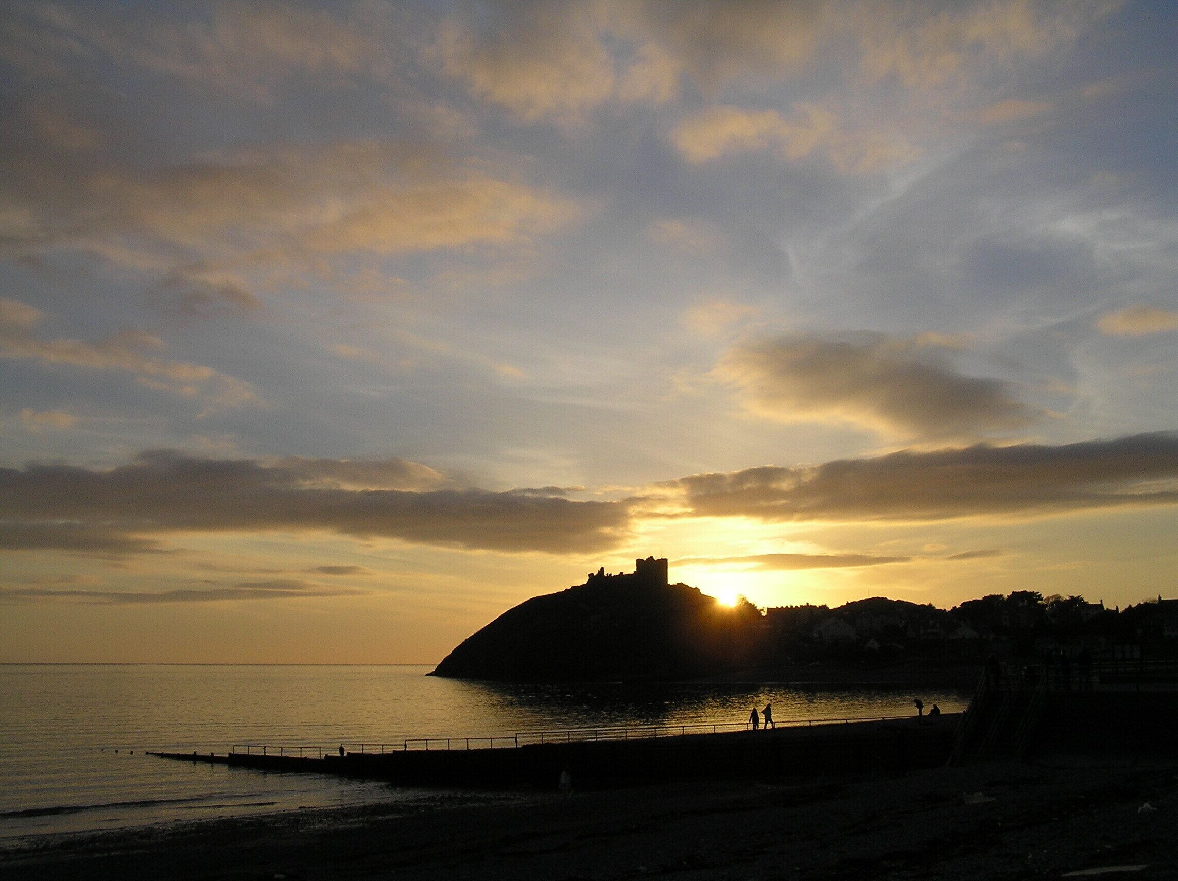 A sunset over a coastal town with a prominent hill and a pier extending into the water.