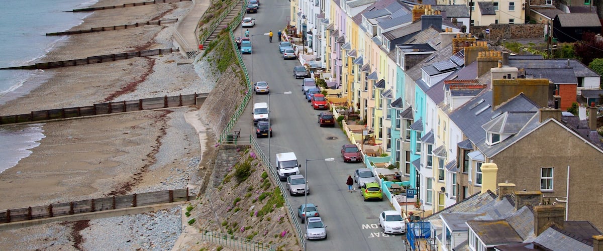 A coastal town with a promenade, colorful houses, and parked cars along the street.