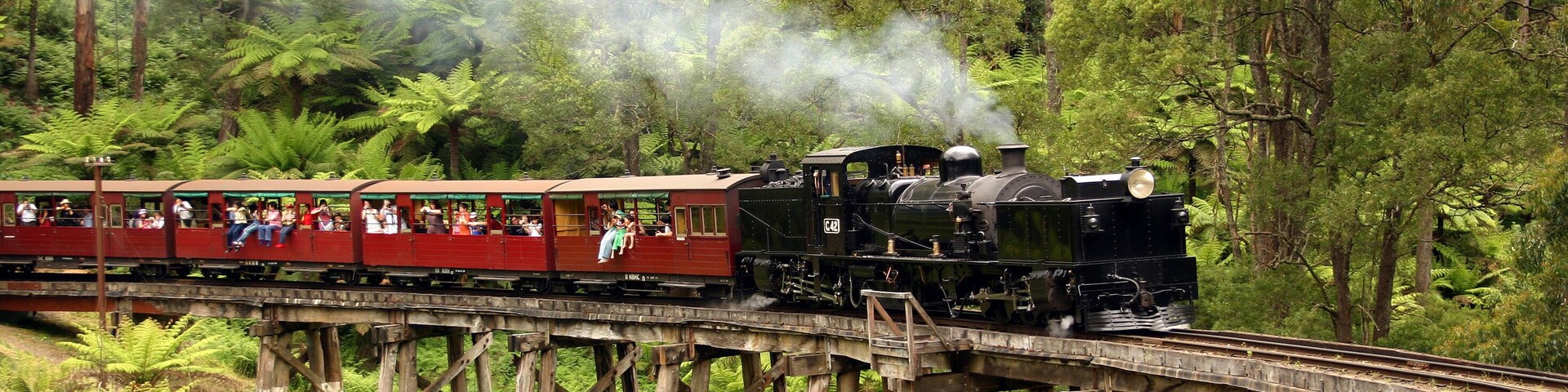 Un tren de vapor sobre un puente de madera atravesando un bosque.