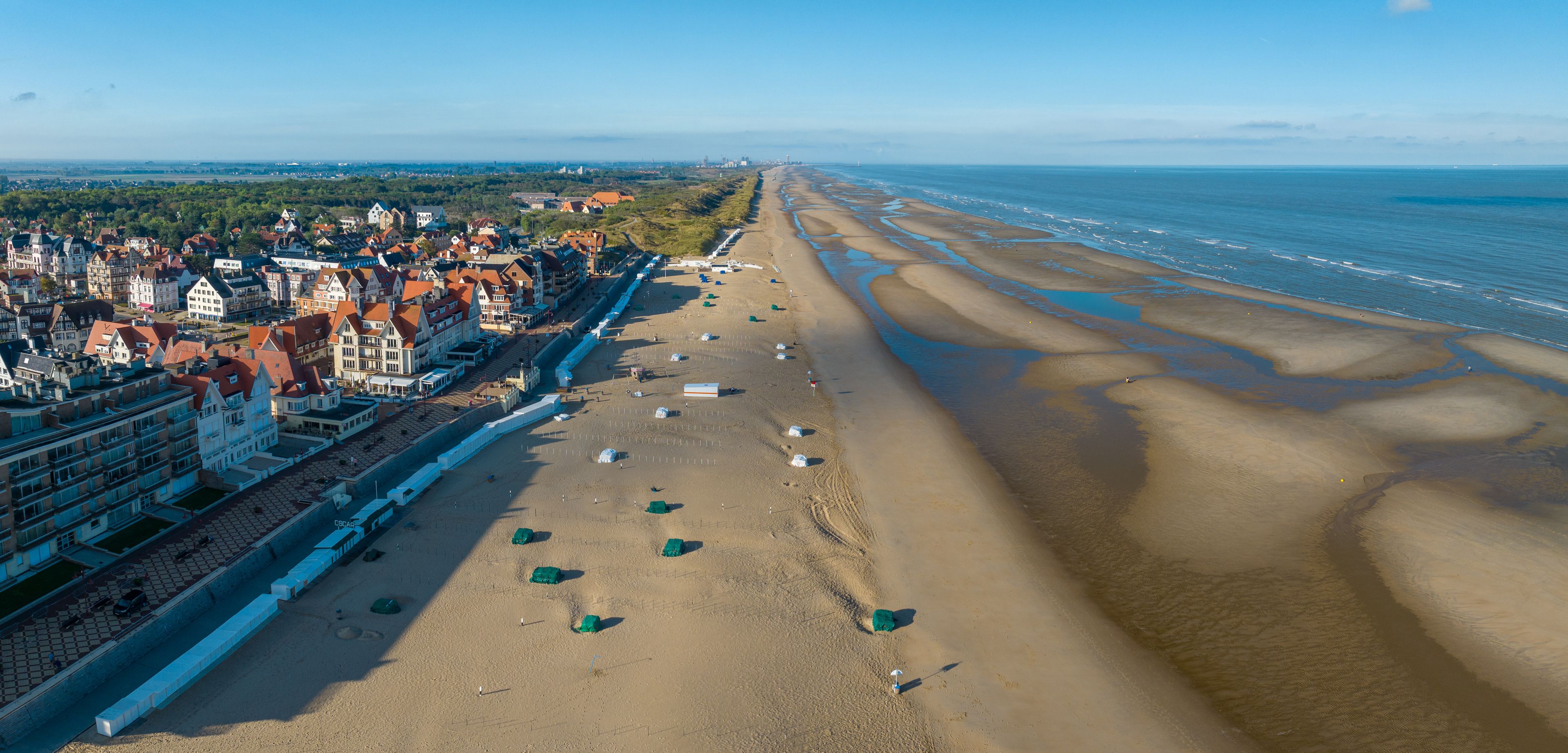 A coastal town with a long sandy beach, a promenade lined with buildings, and a clear view of the sea.