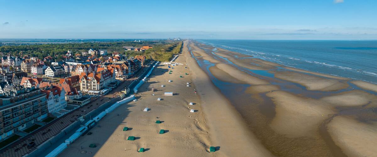A coastal town with a long sandy beach, a promenade lined with buildings, and a clear view of the sea.