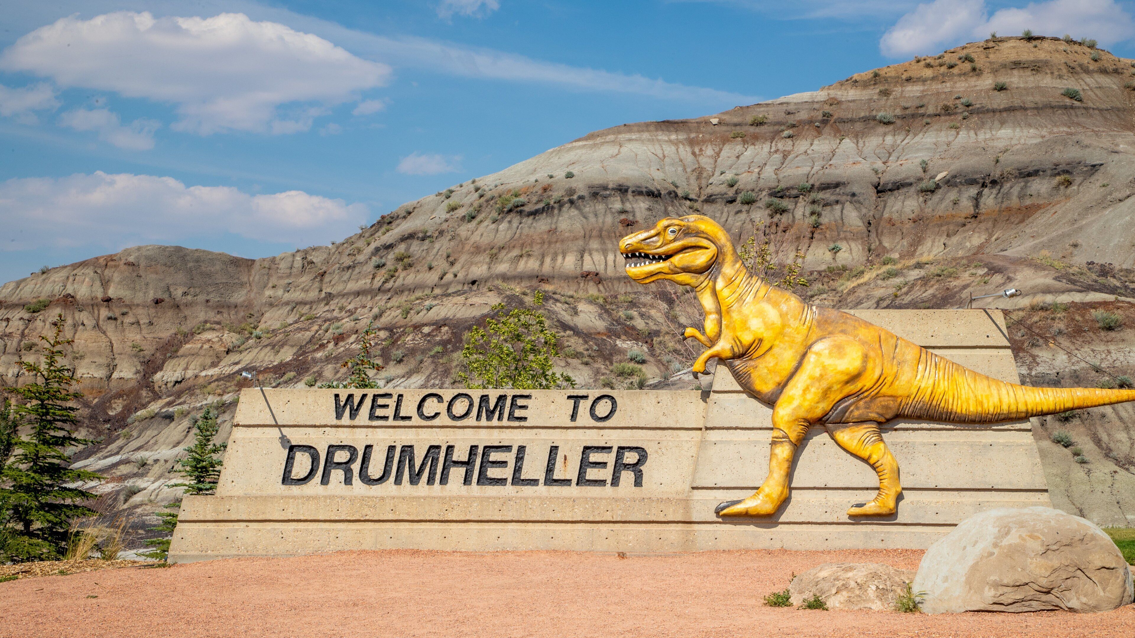 A dinosaur statue and a welcome sign at Drumheller.