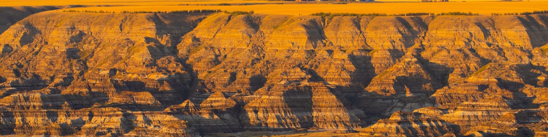 A vast landscape with layered rock formations and a flat field in the foreground.