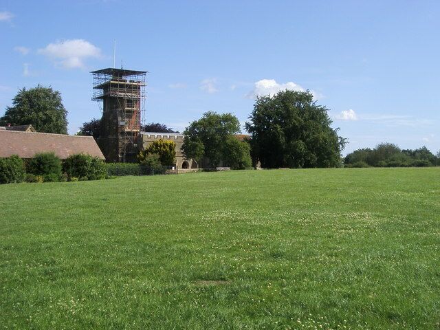 View north across a field to St Mary's parish church, Harlington, Bedfordshire, with scaffolding encasing its west tower
