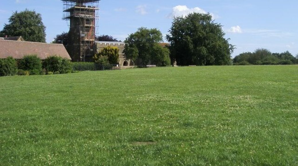 View north across a field to St Mary's parish church, Harlington, Bedfordshire, with scaffolding encasing its west tower