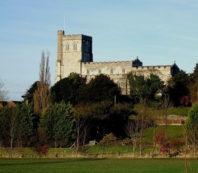 Un castillo histórico con una torre destacada, rodeado de árboles y un campo cubierto de césped.