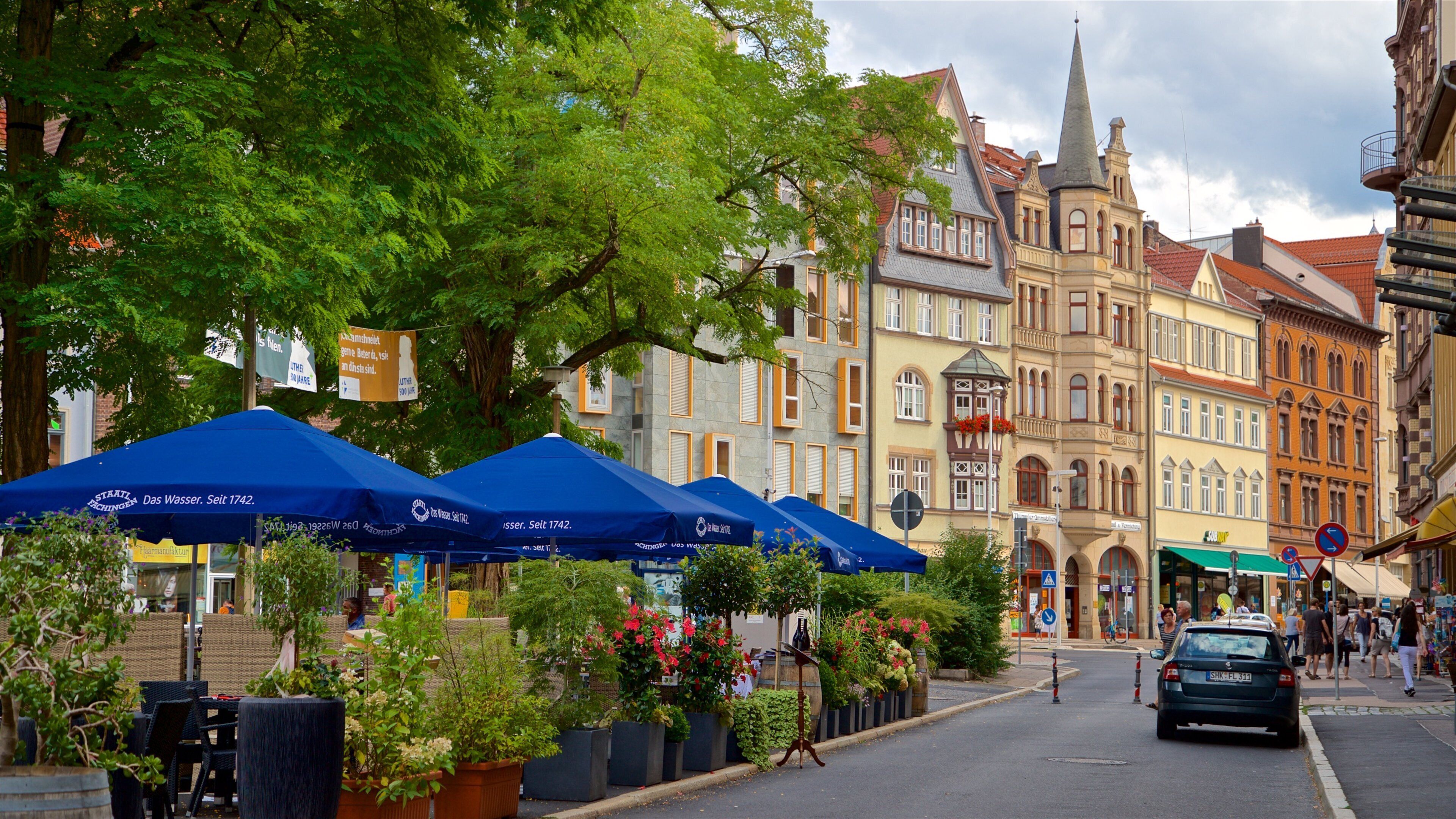 A street lined with historic buildings and blue umbrellas.