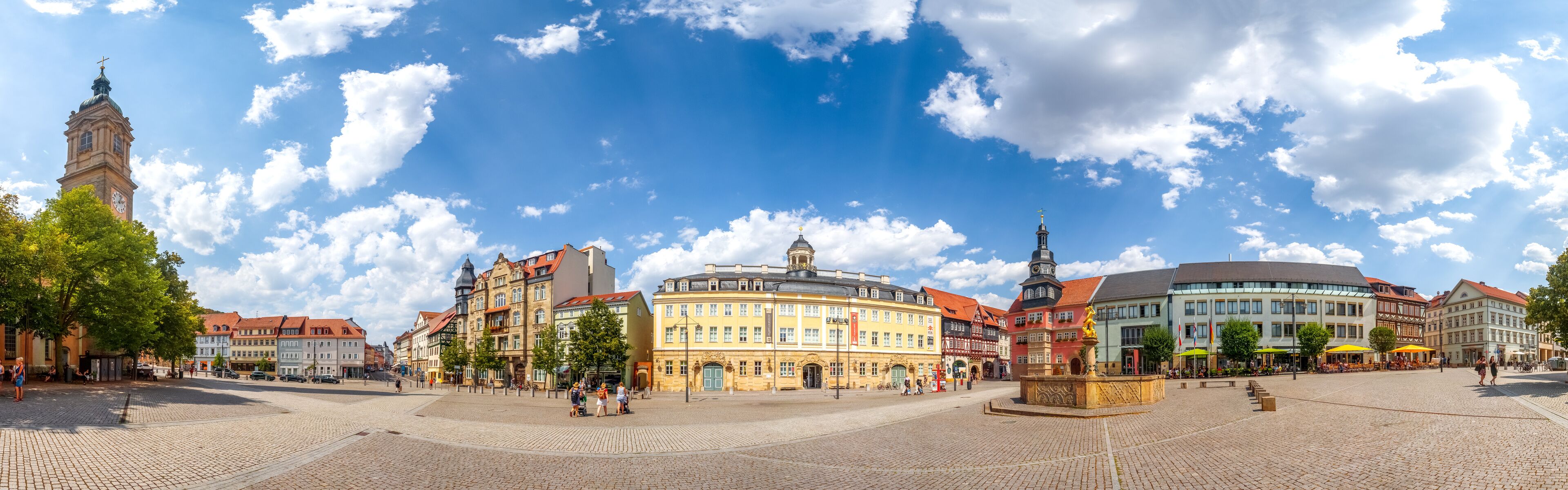 A historic square with cobblestone pavement, a prominent clock tower, and colorful buildings with traditional architecture.