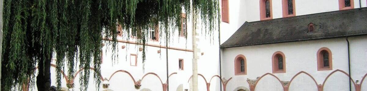 Ein Innenhof mit einem Brunnen, einer Trauerweide und einem Gebäude mit Kuppel und Rundbogenfenstern.