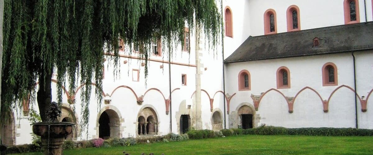 A courtyard with a fountain, a weeping willow tree, and a building with a dome and arched windows.