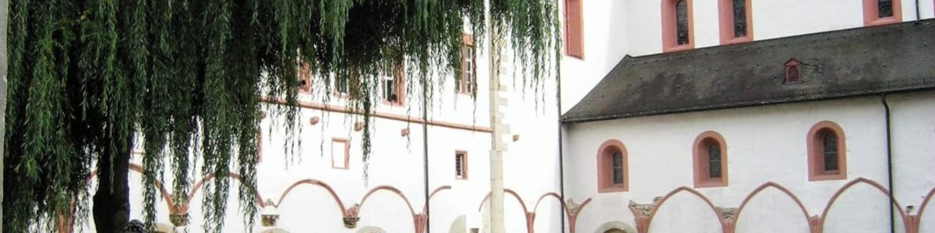 A courtyard with a fountain, a weeping willow tree, and a building with a dome and arched windows.