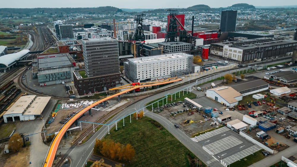 An aerial view of a city with a prominent curved bridge, industrial buildings, and a railway line.