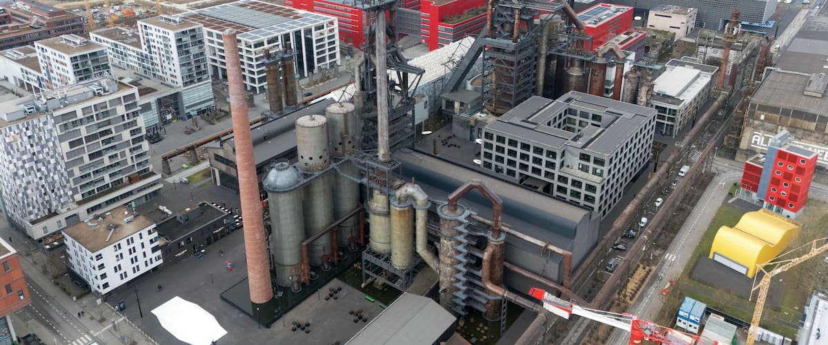 An industrial complex with large buildings, tall chimneys, and extensive piping.
