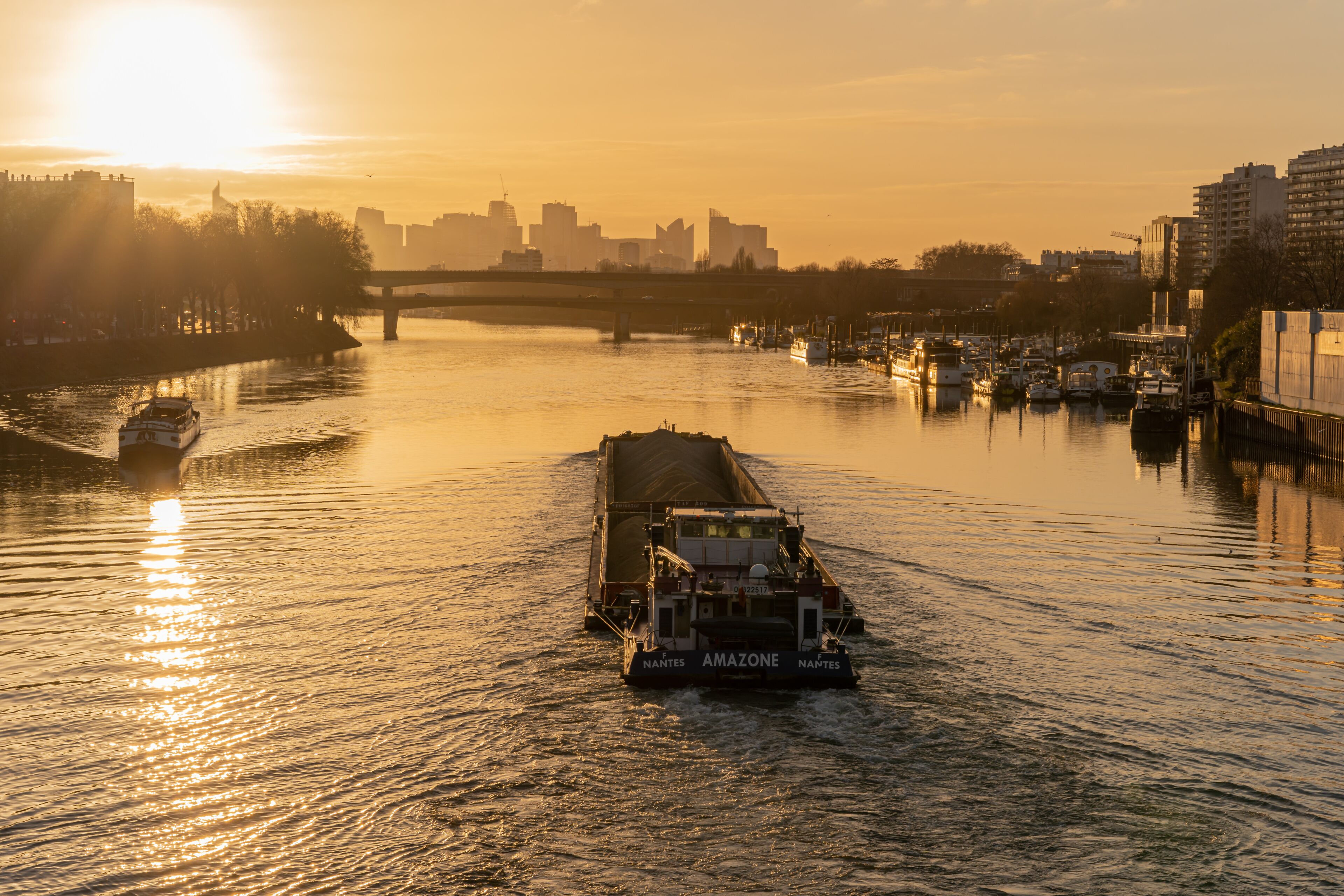 Paris, France - 01 30 2022: Quays of the Seine. View of the freight of a barge sailing along the Seine and The Defense district at sunset from Clichy Bridge