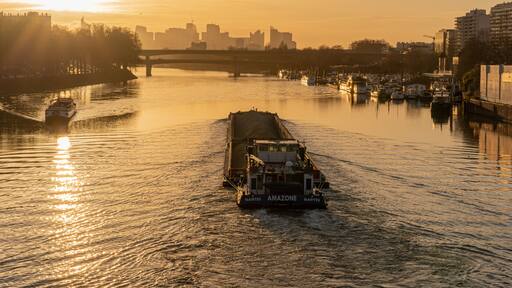 Paris, France - 01 30 2022: Quays of the Seine. View of the freight of a barge sailing along the Seine and The Defense district at sunset from Clichy Bridge
