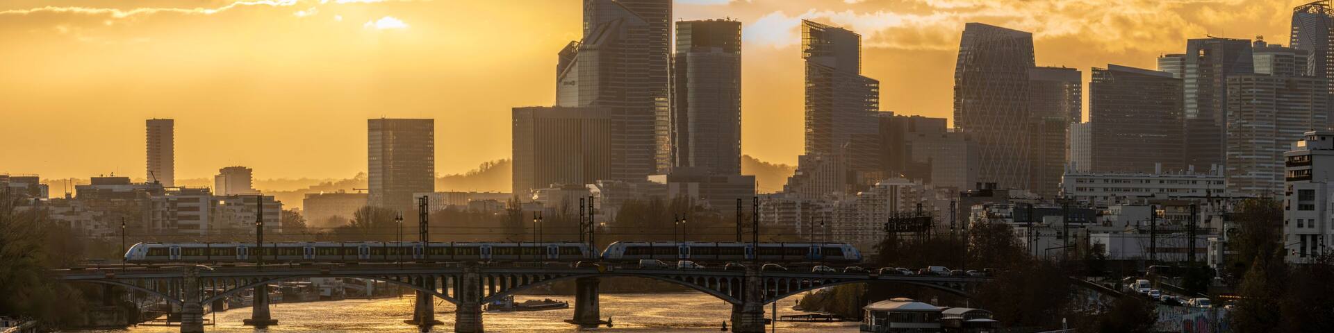 Gennevilliers, France - 11 18 2025: Panoramic view of La Seine river, railway bridge and La Defense towers district in background from Clichy bridge at sunset and golden hour