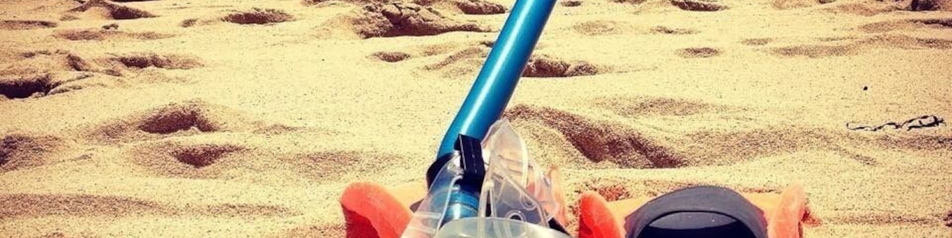 Una persona recostada en una playa arenosa, con un snorkel y antifaz azules, y una bolsa negra cerca.