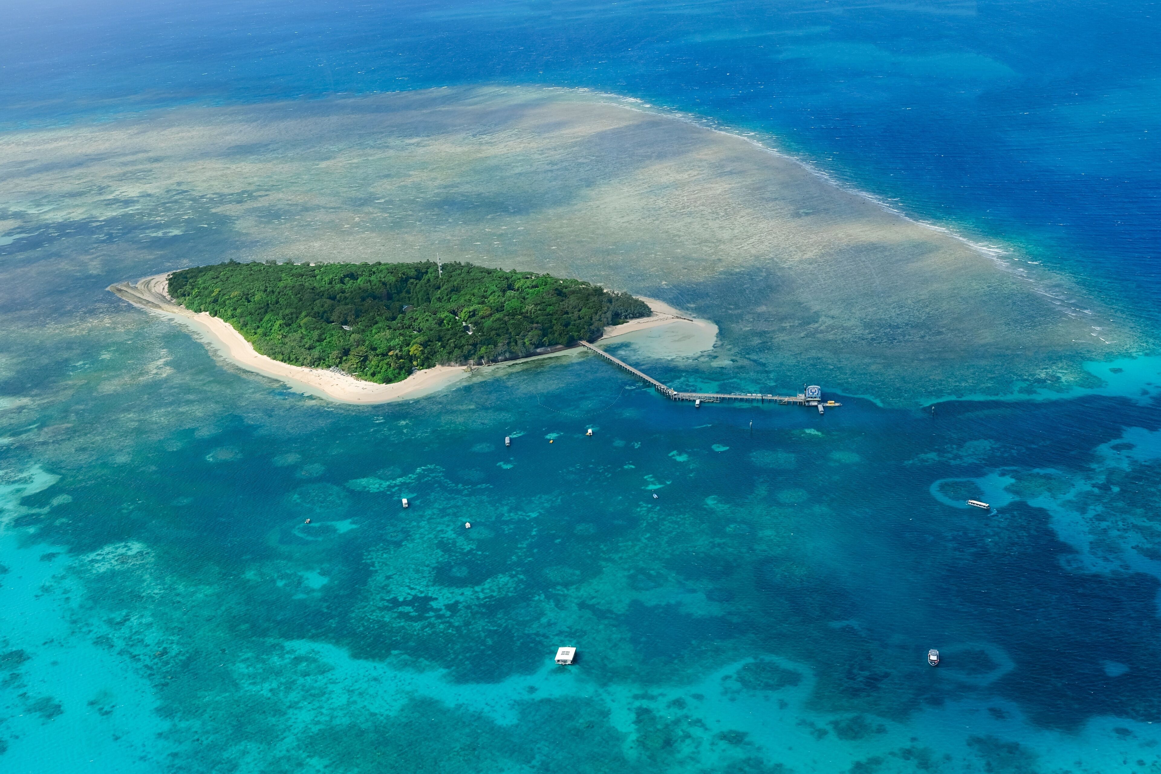 An aerial view of the coral reefs and clear turquoise waters surrounding Green Island, a small tropical isle in the outer Great Barrier Reef — Coral Sea, Cairns; Far North Queensland, Australia