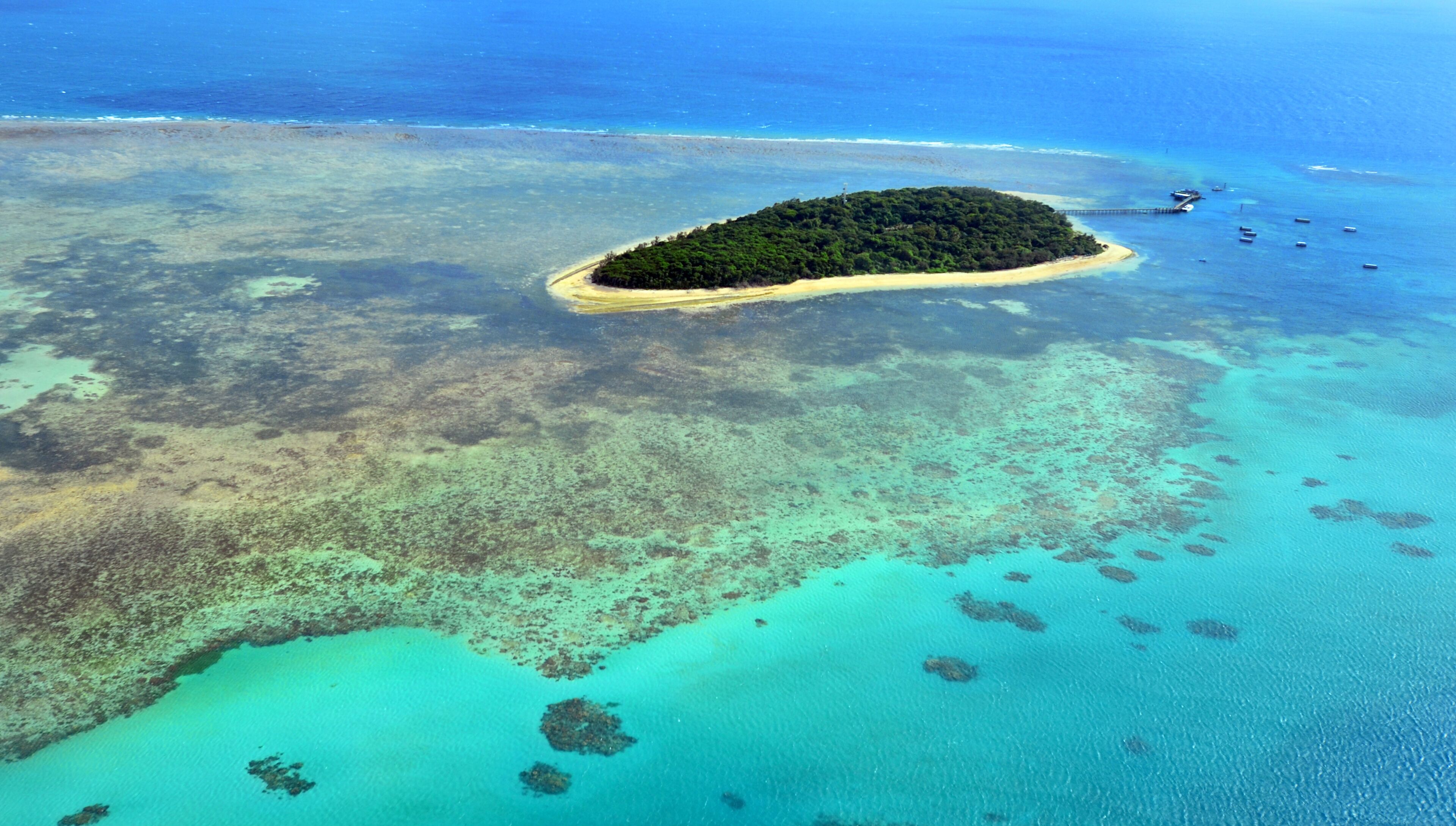 An aerial view of a small island surrounded by clear turquoise waters and coral reefs.