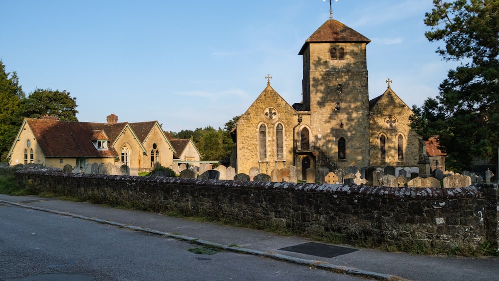 A historic church with a tall bell tower, surrounded by stone walls and smaller buildings.
