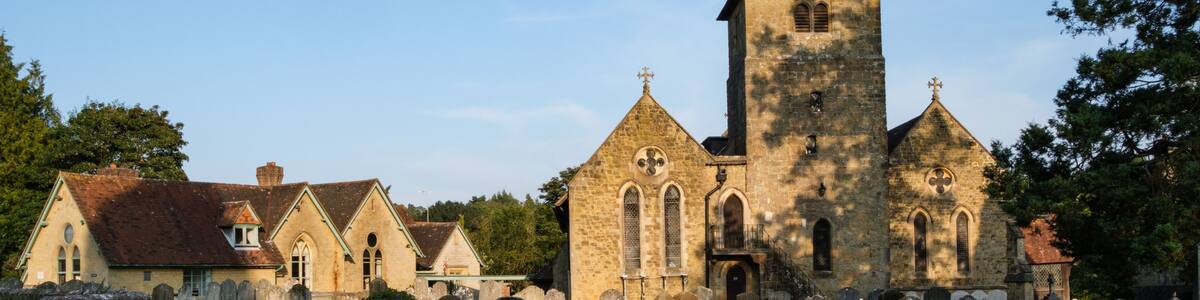 Eine historische Kirche mit einem hohen Glockenturm, umgeben von Steinmauern und kleineren Gebäuden.