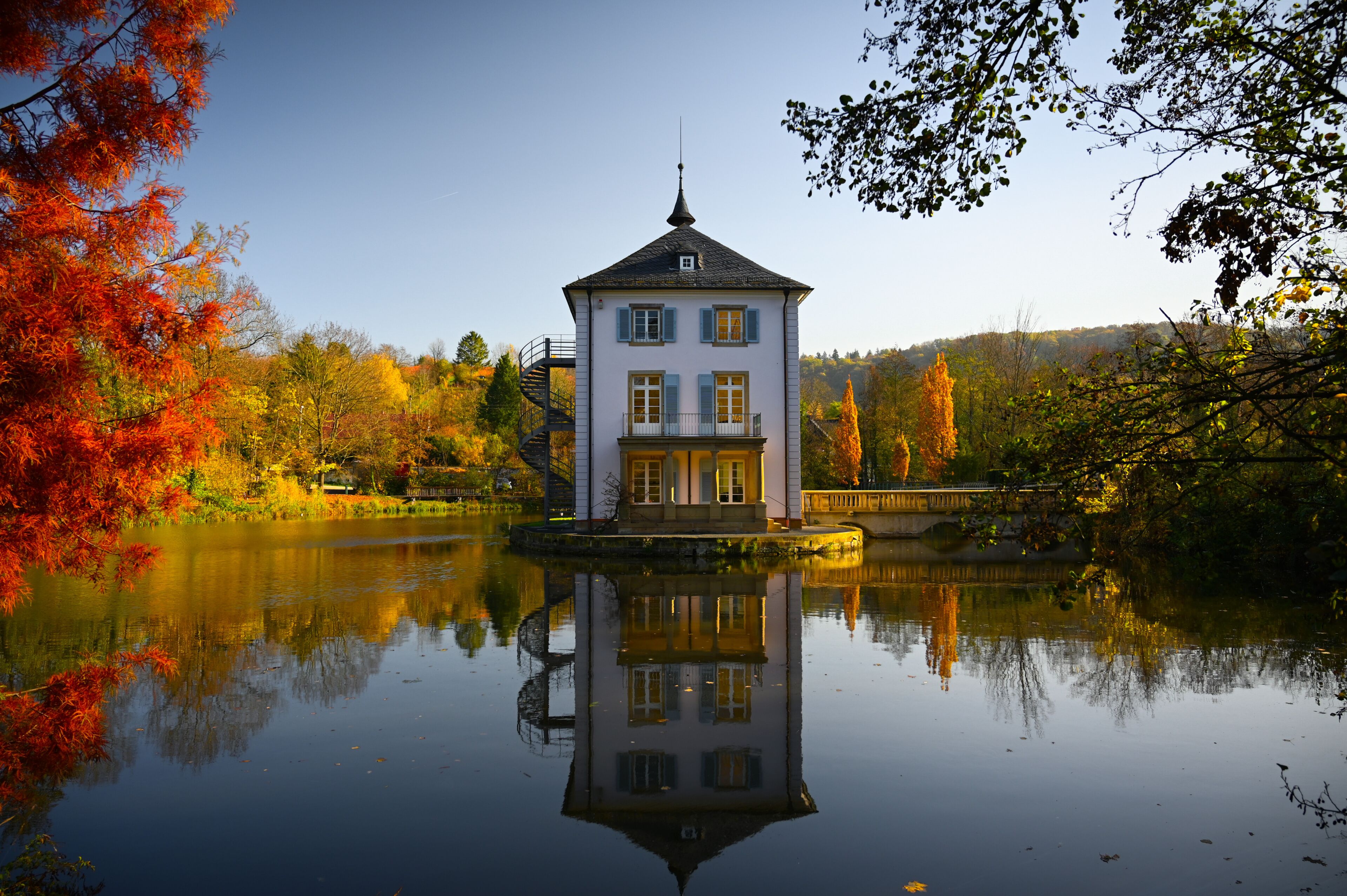 A baroque house, called Trappenseeschlösschen, surrounded by Lake Trappensee in Heilbronn, Germany during autumn. The house and the colorful trees reflect in the water.